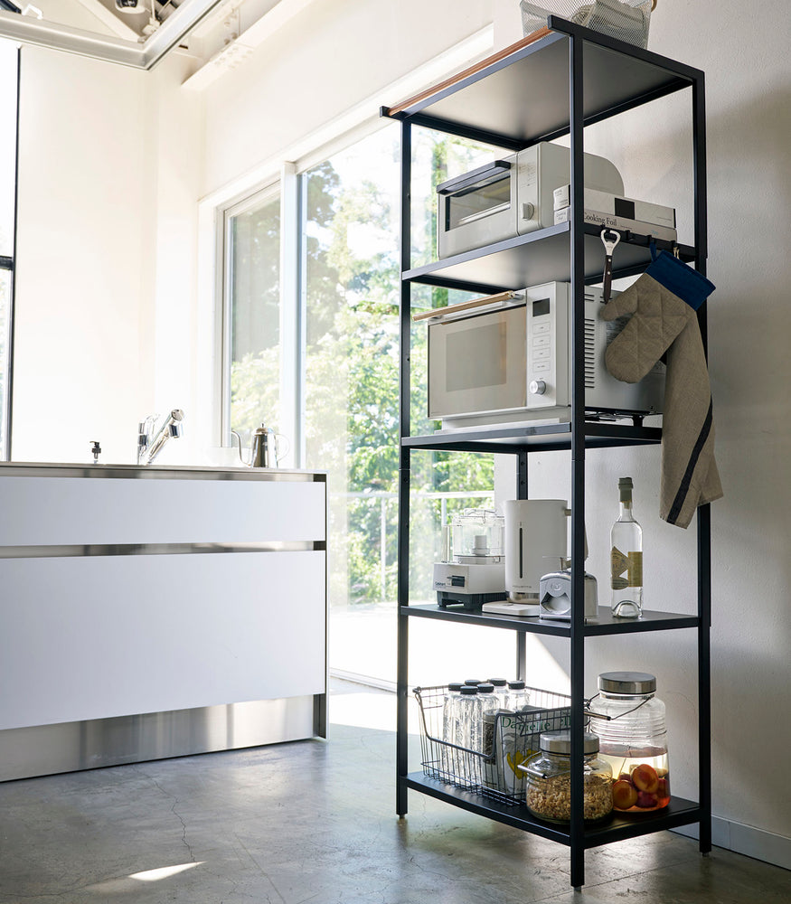 View 28 - Tall black five-tier steel storage rack with a decorative wood accent bar on top shelf and adjustable hooks on sides.