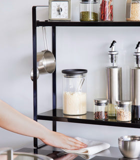 Somone is cleaning up under the Yamazaki Home Two-Tier Countertop Rack holding spices and kitchen utensils. view 13