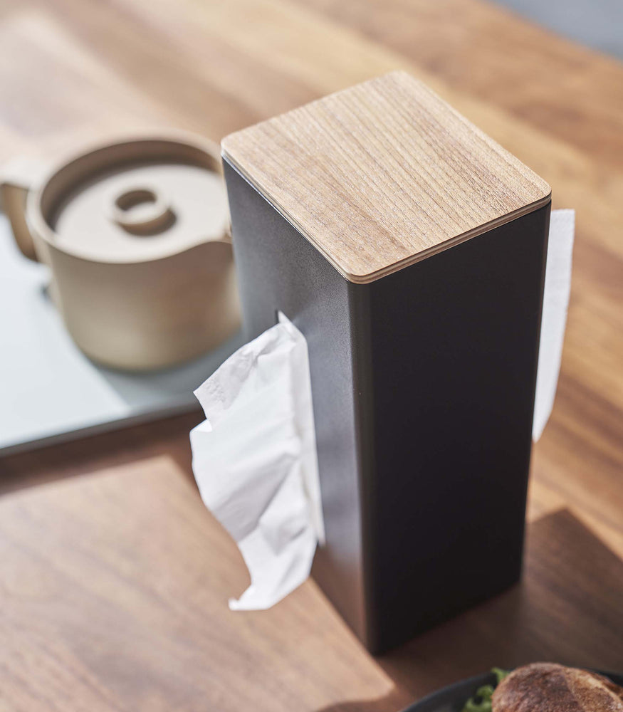 View 13 - Close up of black Yamazaki Two-Sided Tissue Case with tissues inside on a dining table