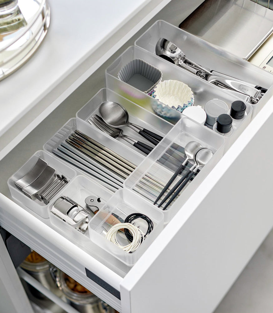 View 52 - Four different sizes of stackable clear organizers —small, medium, large, and deep—are neatly placed in a kitchen drawer. They effectively organize various items such as cutlery, bottle openers, and small trays, showcasing their versatility and stackability