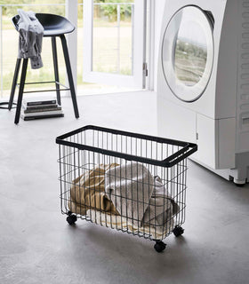 Rolling Wire Basket by Yamazaki Home in black in a sunny laundry room with several towels inside. view 10