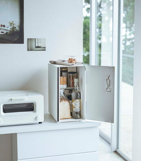 A vertical white metal breadbox is seen on a white kitchen counter next to a white microwave oven and a glass drip coffee pot with a dark liquid inside. view 14
