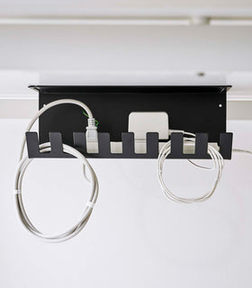 Under-Desk Cable Organizer in black by Yamazaki Home on the bottom of a desk holding cables. view 14