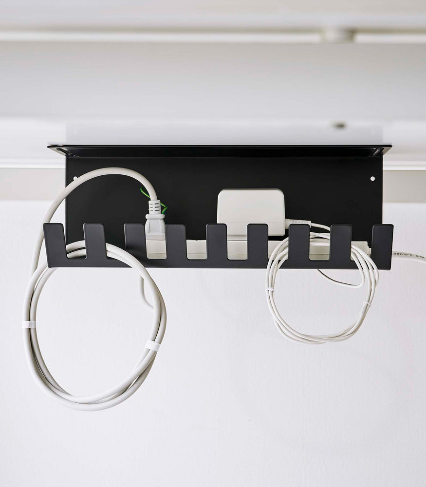 View 14 - Under-Desk Cable Organizer in black by Yamazaki Home on the bottom of a desk holding cables.