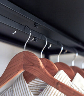 Close up of shirts hung underneath a black Yamazaki Home Expandable Suitcase Rack view 17