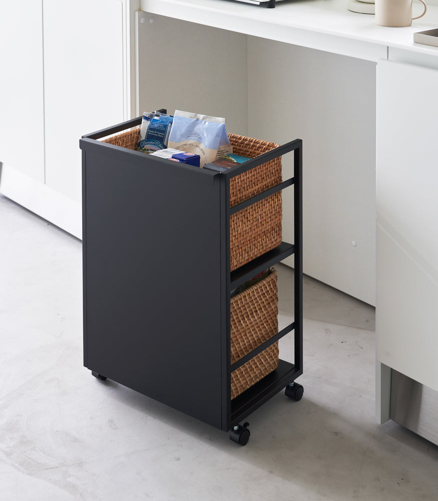 View 14 - Two-level black steel storage cart with casters is shown in an opening of a recessed cabinet. Cart houses storage bins on both levels. Side with a solid wall is facing the camera concealing the storage bins.