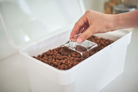 Close up view of person using clear measuring cup scooping pet food from white Airtight Food Storage Container by Yamazaki Home. view 6