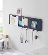 Yamazaki black Magnetic Wall Panel with things pinned to it as well as kitchen utensils hanging from hooks