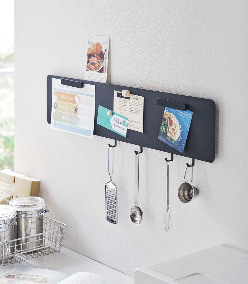 Yamazaki black Magnetic Wall Panel with things pinned to it as well as kitchen utensils hanging from hooks