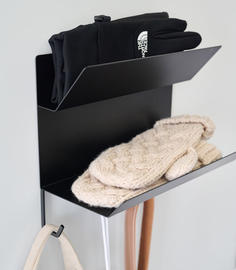 Close-up of the shelves on the Magnetic Entryway Rack by Yamazaki Home in black. Various entryway items are stored on the rack including gloves and a dog leash.