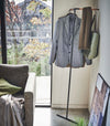 Yamazaki black Corner Leaning Coat Hanger placed in the corner of a room with items hung on it