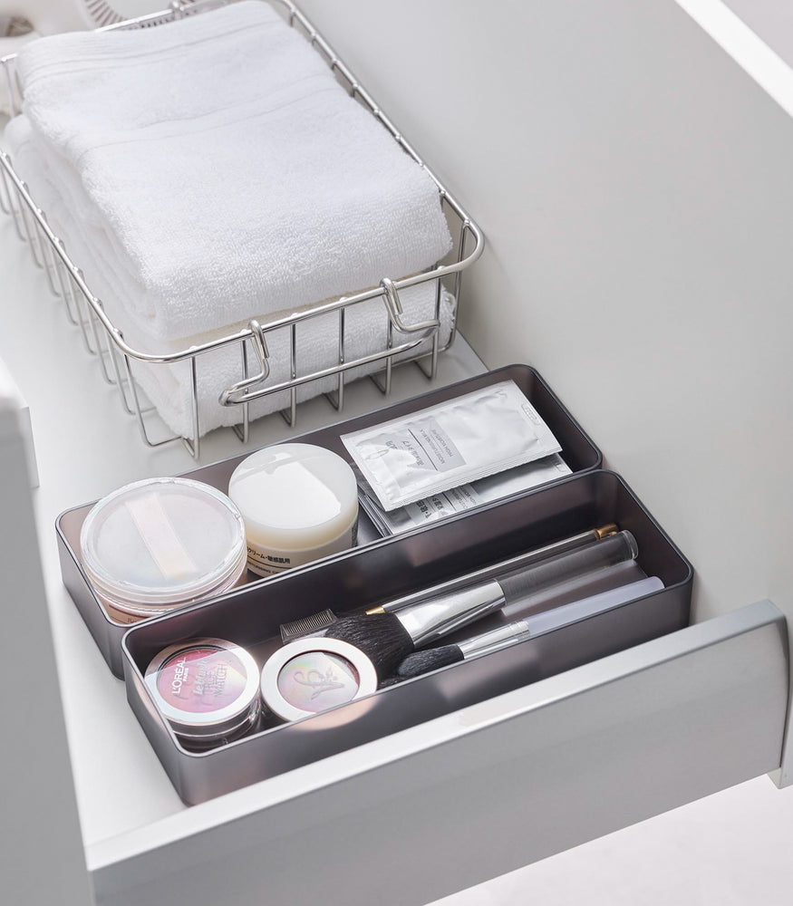 View 42 - Two large stackable clear organizers in black are placed in a bathroom drawer, organizing cosmetic items and brushes, neatly placed next to each other.