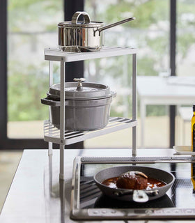 White Two-Tier Corner Riser holding pot and saucepan next to stovetop by Yamazaki Home. view 2