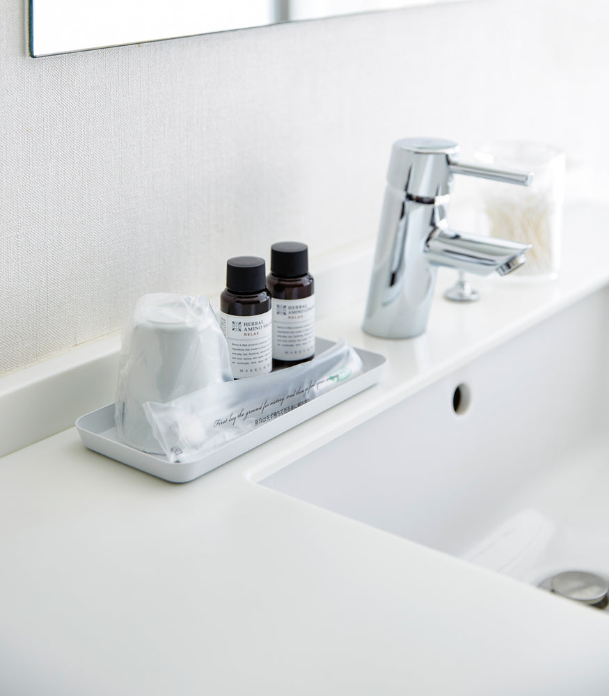 View 13 - Flat white Accessory Tray holding soap, cup, and toothbrush on bathroom sink countertop by Yamazaki Home.
