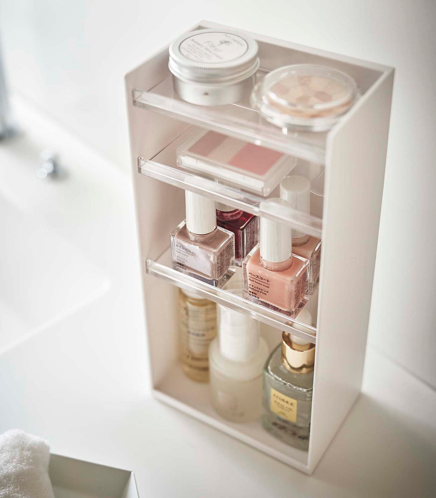 View 3 - White Cosmetics Storage Tower by Yamazaki Home holding nail polish and other cosmetic items.