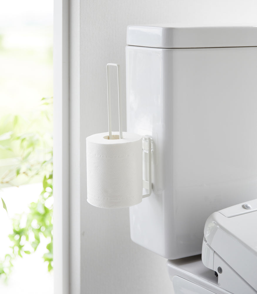 View 3 - White Yamazaki Home Traceless Adhesive Toilet Paper Holder on a toilet with a toilet paper roll stored