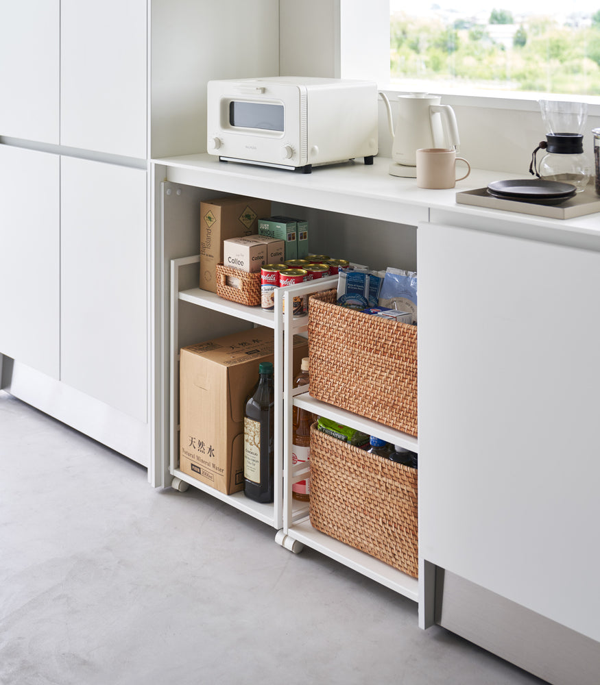 View 6 - Two two-level white steel storage carts with casters are shown in an opening of a recessed cabinet. One cart houses two storage bins, the other houses food supplies on one level and a box and larger liquids on the other.