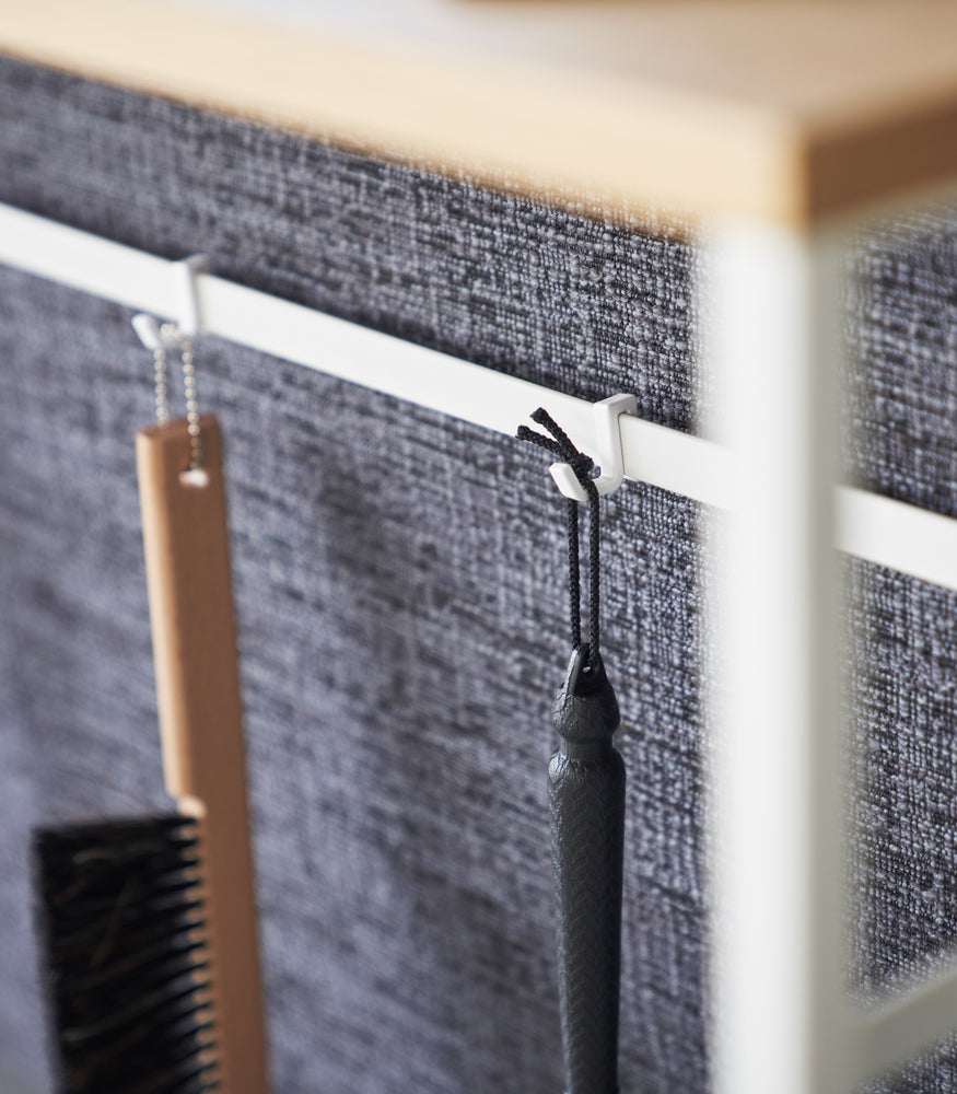 View 6 - Items hanging form hooks on the back bar of the Long Console Table by Yamazaki Home in white.