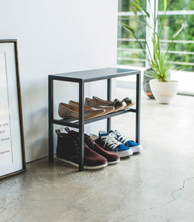 Black two-tier steel shoe rack with flat metal surface on top. view 15