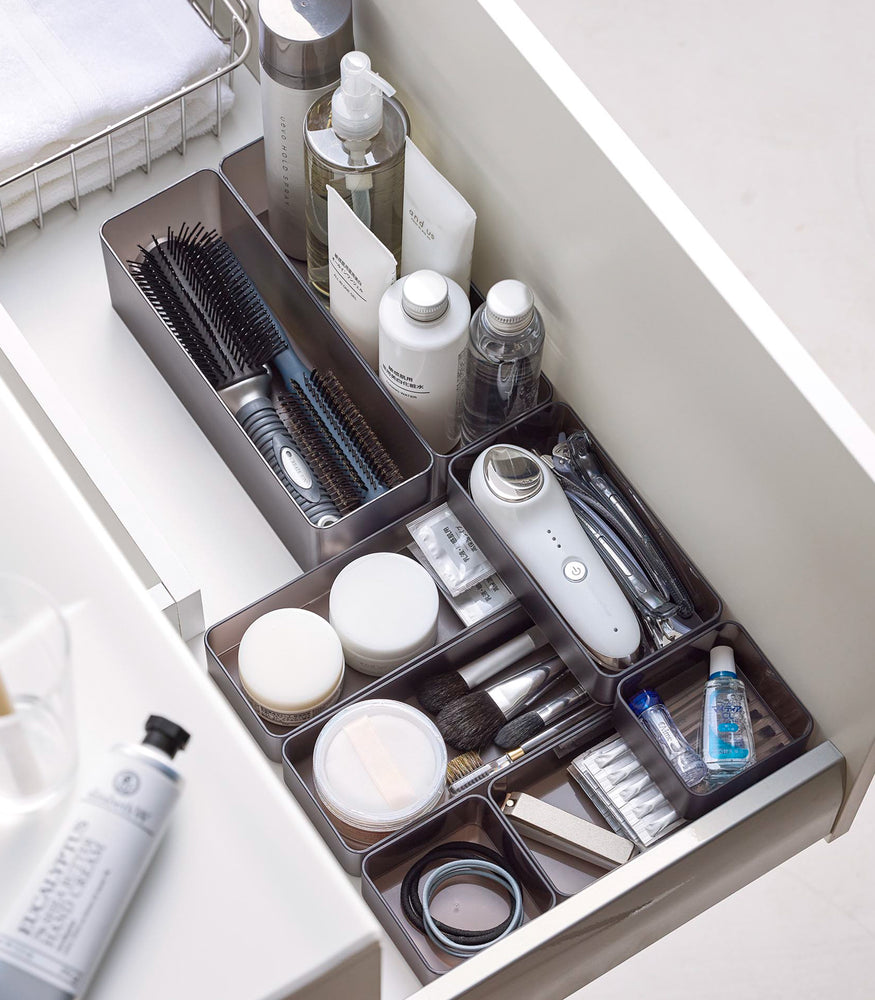 View 25 - Four different sizes of stackable clear organizers in black —small, medium, large, and deep—are neatly placed in a bathroom drawer. Made from transparent material, they accommodate items like brushes and sanitary products, showcasing their clarity and stackability.