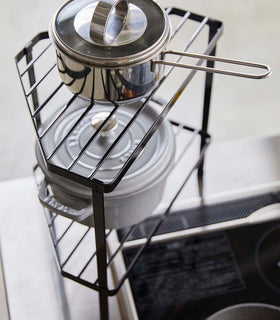 Aerial view of Black Two-Tier Corner Riser holding pot and saucepan in kitchen by Yamazaki Home. view 10