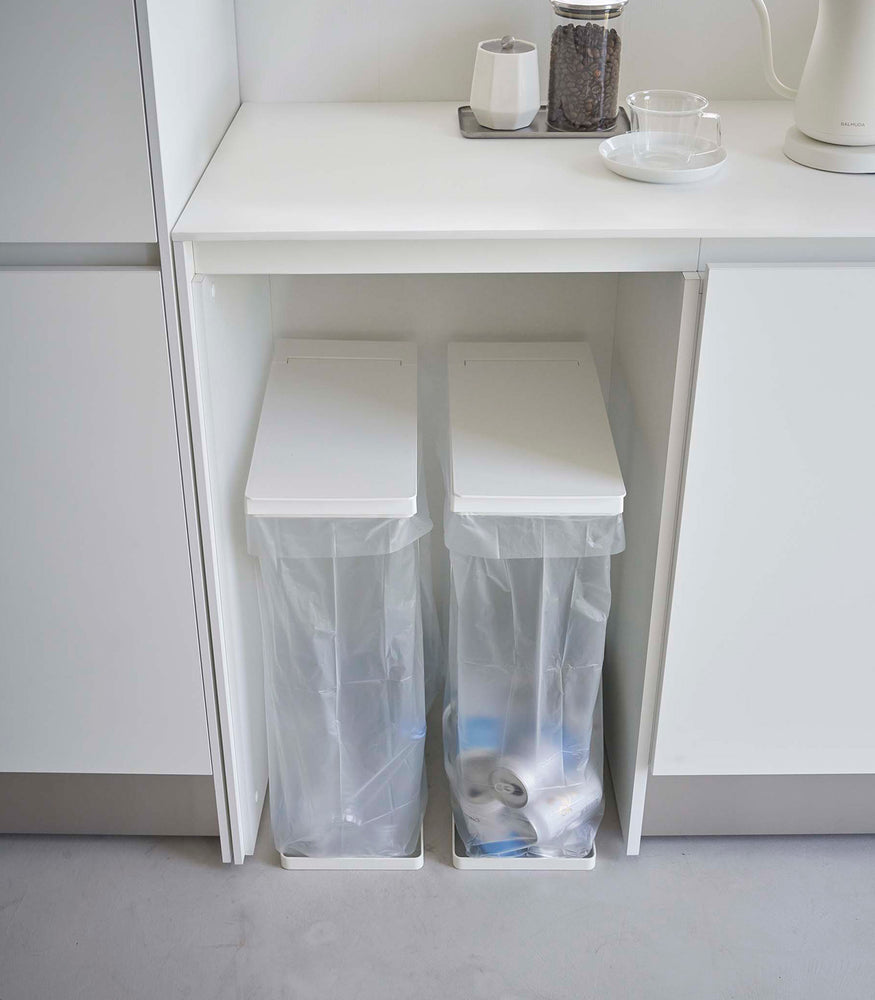 View 5 - Two white Yamazaki Home Lidded Garbage Bag Holder under a shelf