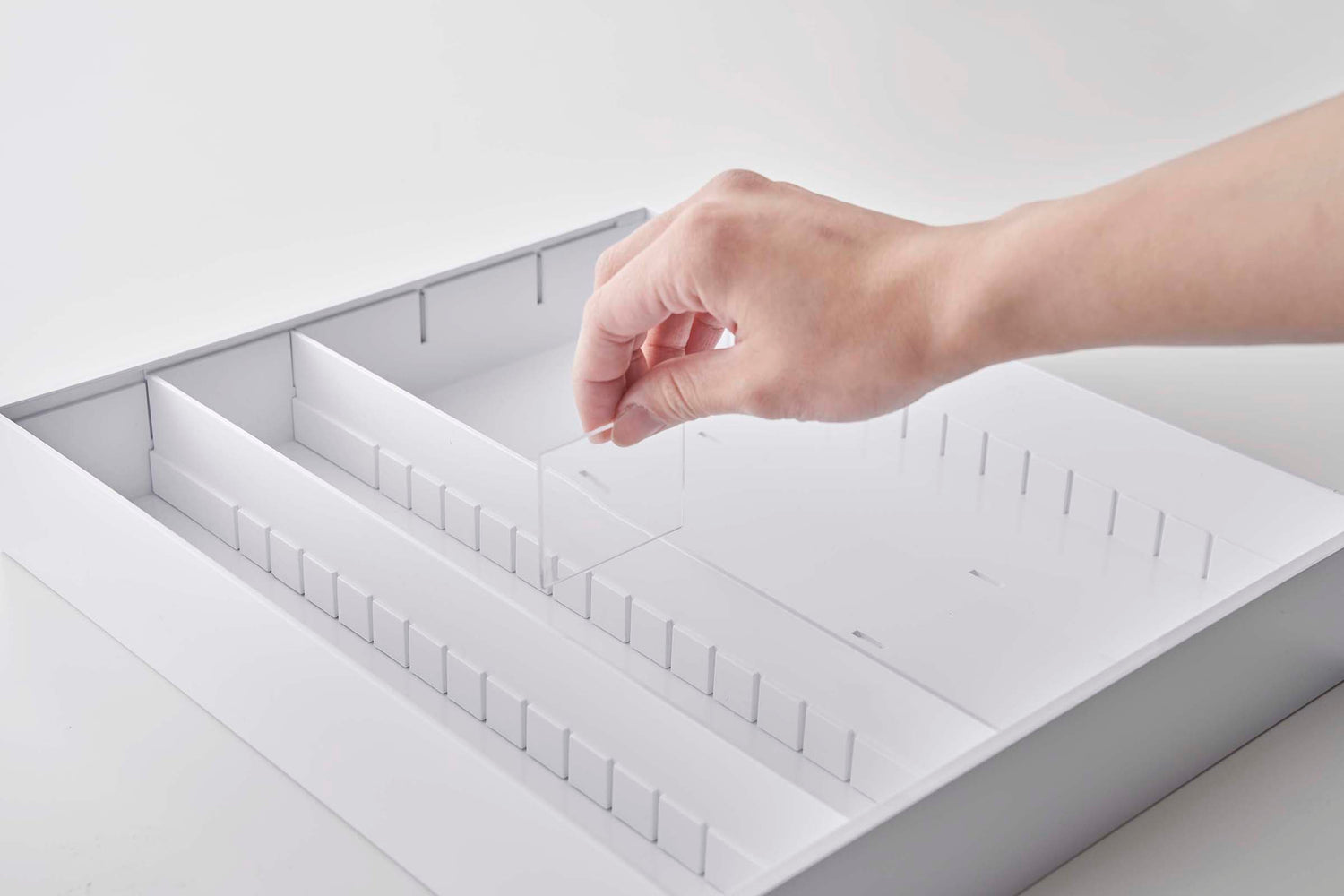 View 19 - Person inserting dividers in white Expandable Cutlery Storage Organizer on white background by Yamazaki Home.