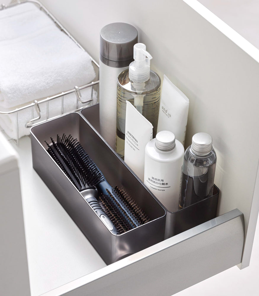 View 58 - Two deep stackable clear organizers in black are placed in a bathroom drawer, organizing brushes and bottles of cosmetics, neatly placed next to each other.