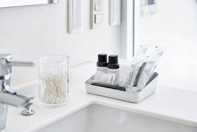 Angeled front view of medium white Accessory Tray holding beauty items on bathroom sink counter by Yamazaki Home. view 4