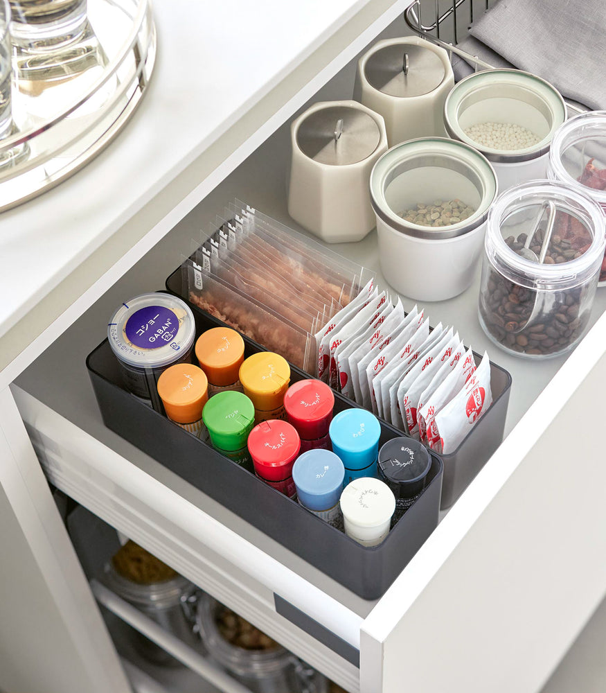 View 56 - Two deep stackable clear organizers in black are placed in a kitchen drawer, organizing bins and pouches of spices, neatly placed next to each other.