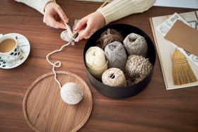 Yamazaki Home large black Storage Case with balls of yarn inside on a dining table beside a cup of coffee and a person knitting view 25