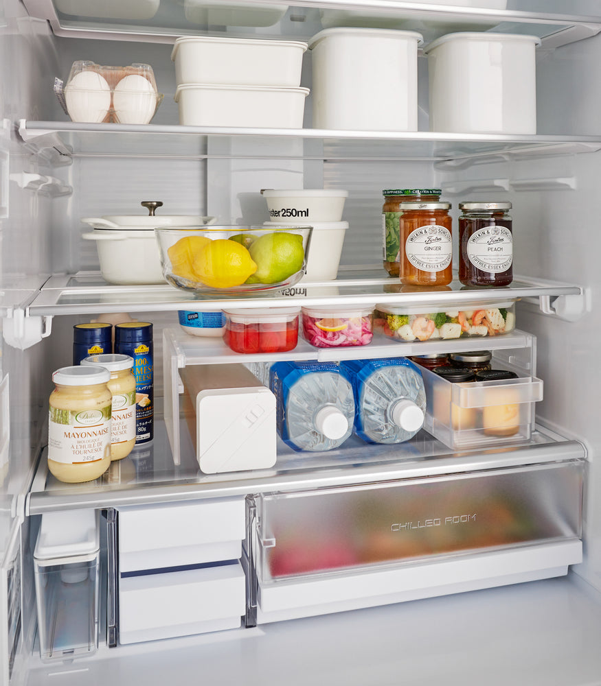 View 3 - Yamazaki Home’s white Expandable Refrigerator Riser Shelf shown inside a fridge with various containers, effectively creating additional shelf space."