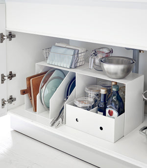 Side view of White Under-Cabinet Storage Shelves holding bowls and baskets on the top and oils and pans underneath under a sink.