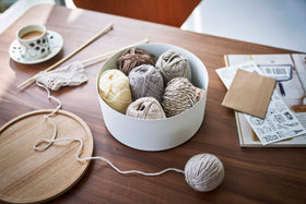 Yamazaki Home large white Storage Case with balls of yarn inside on a dining table next to a cup of coffee and knitting needles view 19
