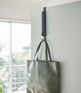 Black Yamazaki Home Folding Over-The-Door Hanger closed with a purse hung view 21
