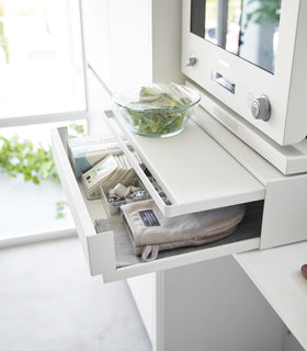 A sidel view of the Countertop Drawer with Pull-Out Shelf by Yamazaki Home in white with both the drawer and shelf pulled out. The drawer contains food wraps, tea items, and an oven mitt among other items. A countainer of food is set on the pulled out shelf. view 6