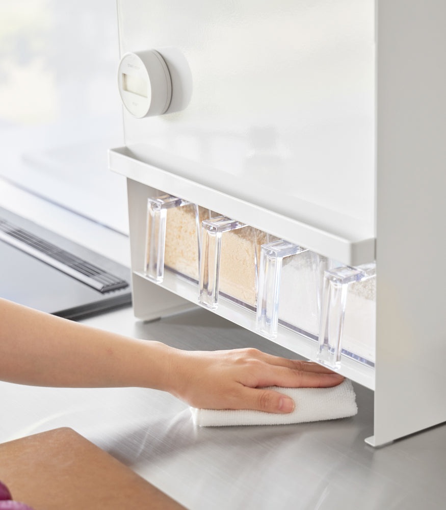 View 5 - Image of a hand holding a duster and cleaning the countertop area under the Concealable Spice Rack by Yamazaki Home in white.