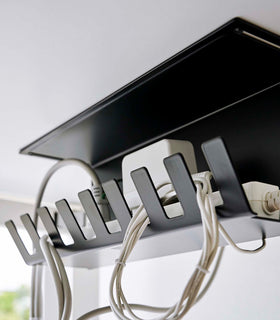 Close-up of Under-Desk Cable Organizer in black by Yamazaki Home mounted under a desk holding a power strip. view 13