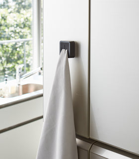 Black Yamazaki Home Traceless Adhesive Towel Holder attached to a cabinet with a towel inserted view 10
