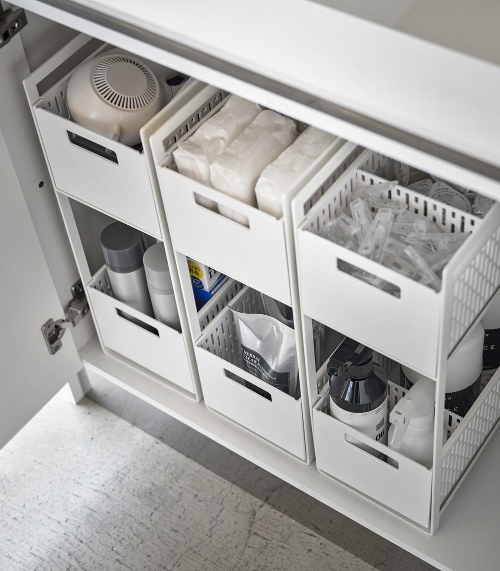 Three two-tier storage bins are displayed in an under-a-sink cabinet. Both levels of each hold various cleaning products and supplies.