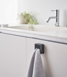 Black Yamazaki Home Traceless Adhesive Towel Holder attached to a cabinet under a sink with a towel inserted view 15