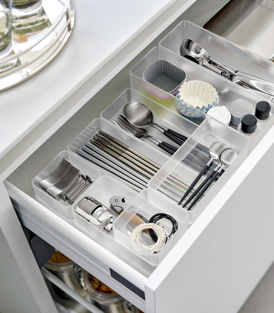 View 6 - Four different sizes of stackable clear organizers—small, medium, large, and deep—are neatly placed in a kitchen drawer. They effectively organize various items such as cutlery, bottle openers, and small trays, showcasing their versatility and stackability