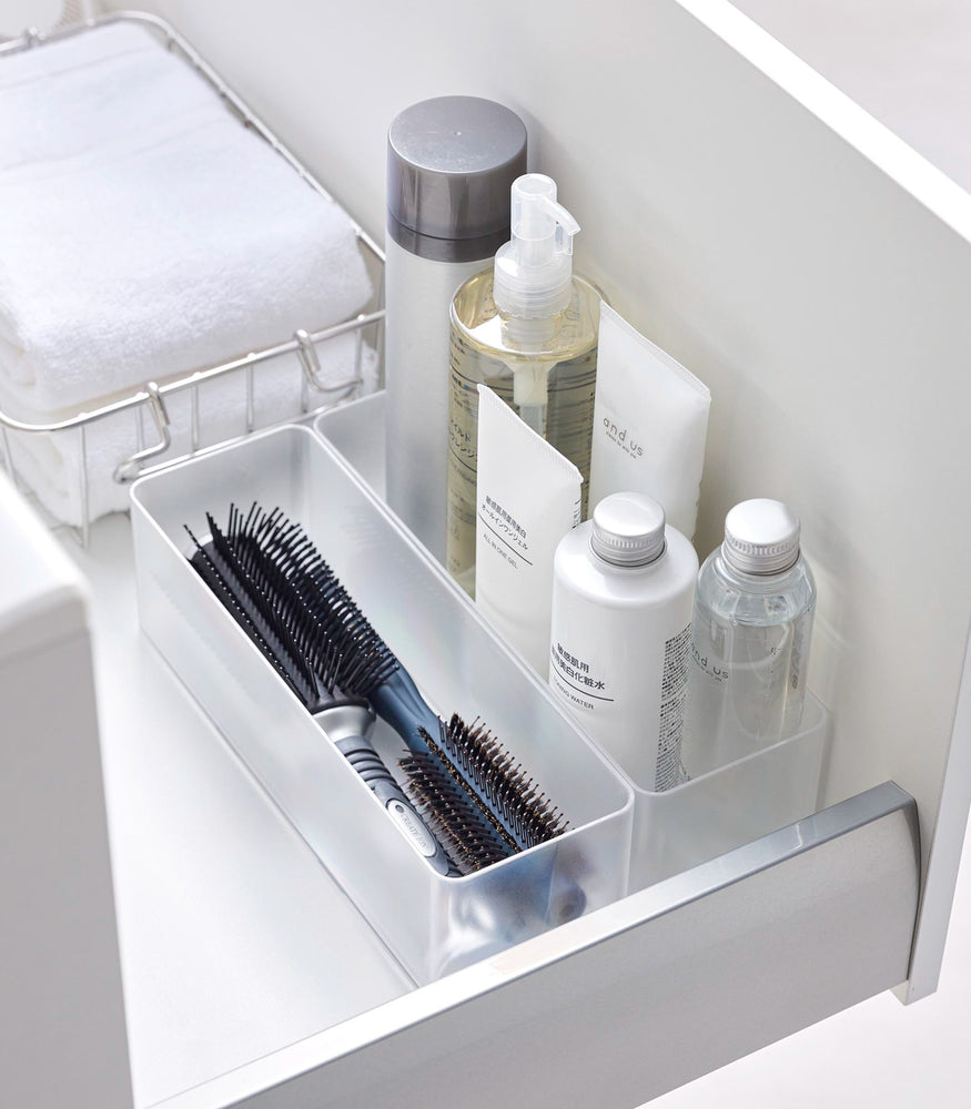 View 50 - Two deep stackable clear organizers are placed in a bathroom drawer, organizing brushes and bottles of cosmetics, neatly placed next to each other.