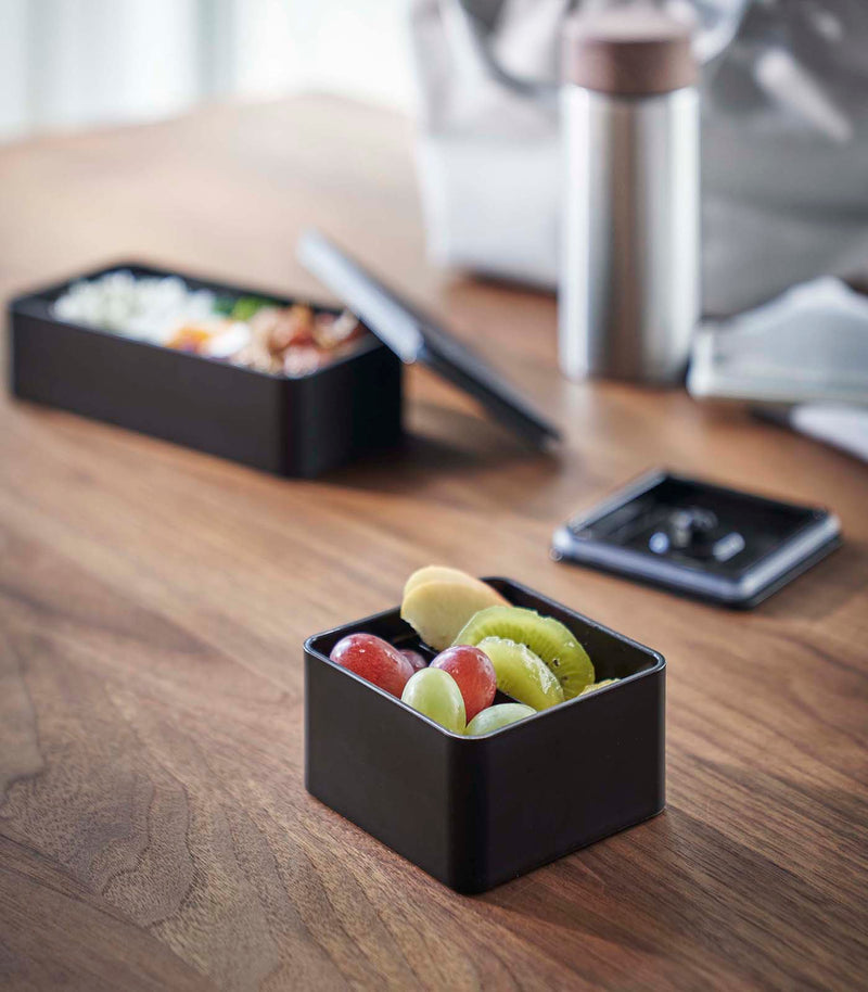 Black Vacuum-Sealing Bento Box holding fruit on table by Yamazaki Home.