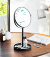 Black Vanity Mirror holding watch, rings, and perfume on table by Yamazaki Home.