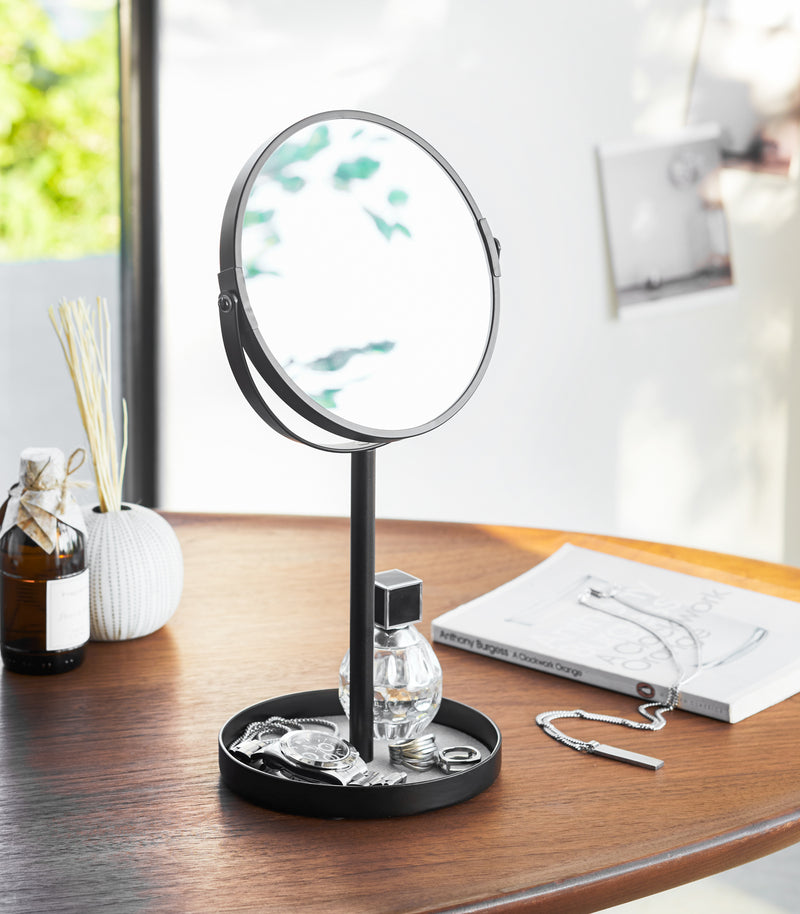 Black Vanity Mirror holding watch, rings, and perfume on table by Yamazaki Home.