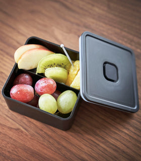 Close up aerial view of black Vacuum-Sealing Bento Box with cover ajar holding fruit by Yamazaki Home. view 10