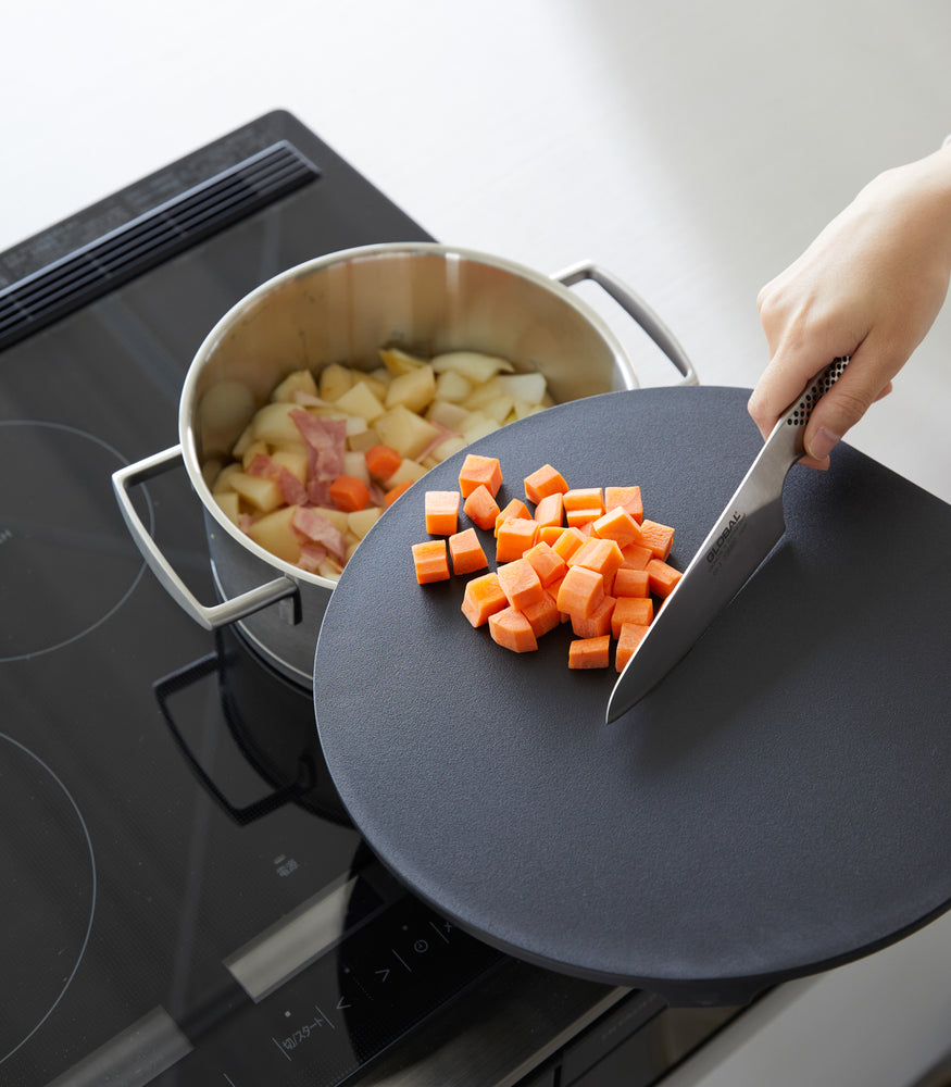 View 14 - A black Yamazaki Round Magnetic Cutting Board being used to cut carrots.