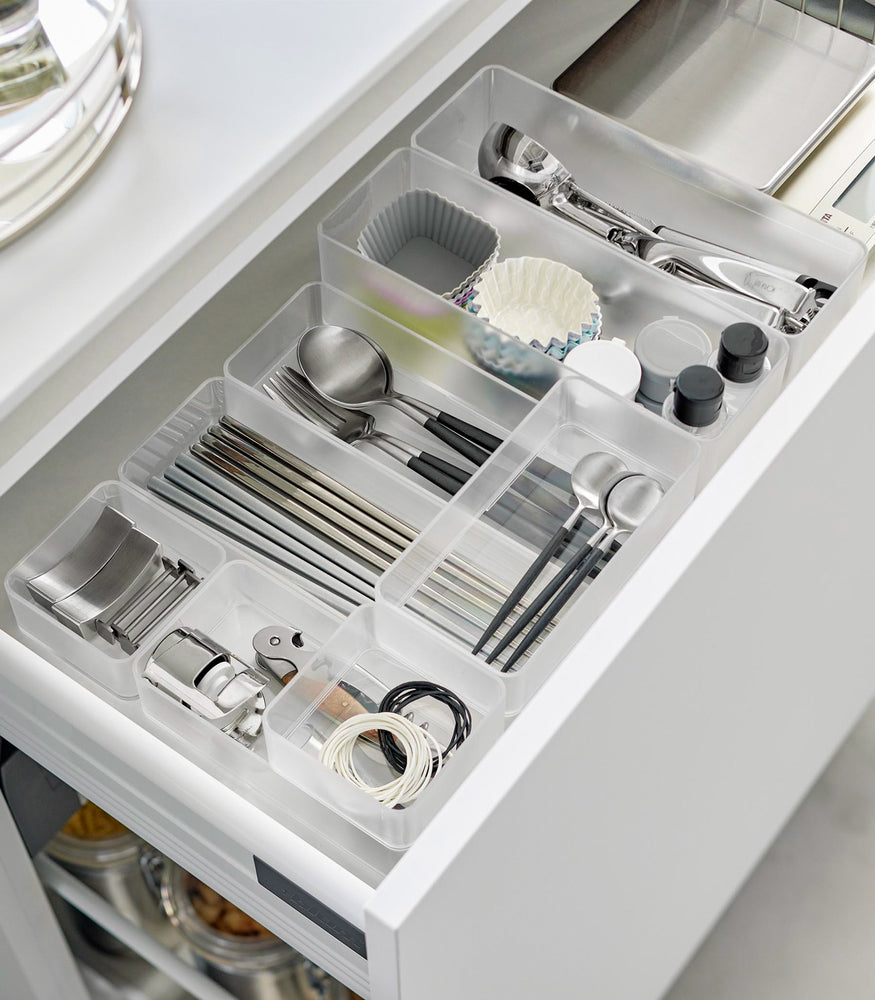 View 20 - Four different sizes of stackable clear organizers—small, medium, large, and deep—are neatly placed in a kitchen drawer. They effectively organize various items such as cutlery, bottle openers, and small trays, showcasing their versatility and stackability