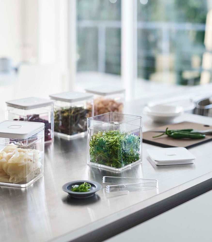 View 2 - White Vacuum-Sealing Food Container w. Tongs on kitchen countertop and holding food items by Yamazaki Home.